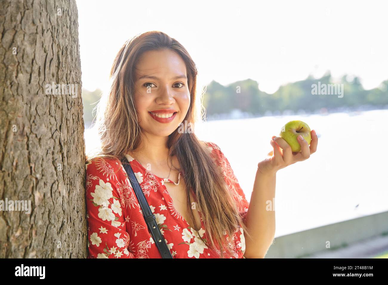 Porträt einer jungen Latina in einem Park mit einem grünen Apfel in ihren Händen. Frau mit perfekten Zähnen und einem großen Lächeln, die ihre Freizeitaktivitäten genießt. Stockfoto