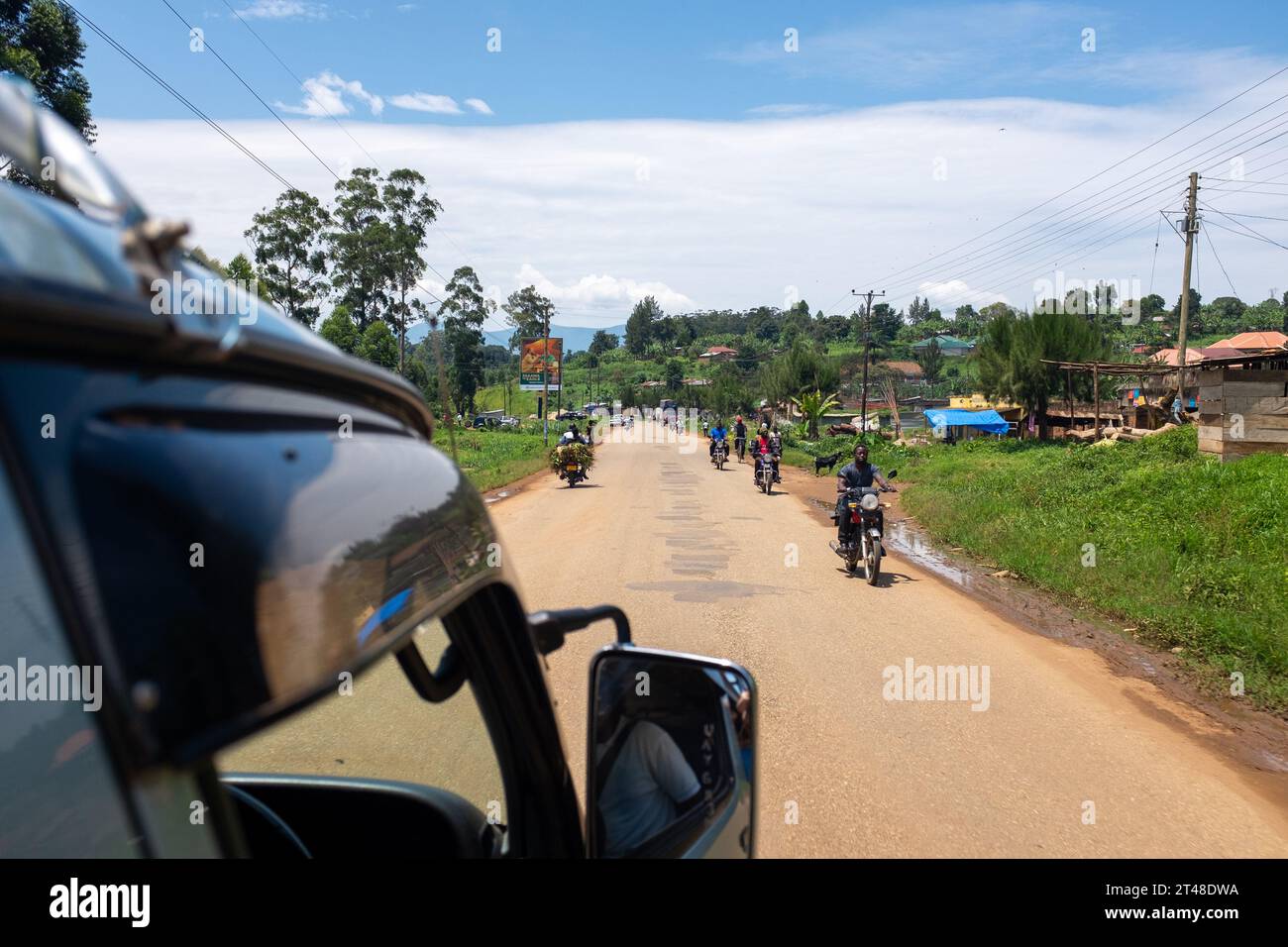 Ein Kleinbus fährt entlang der Straße am Stadtrand von Fort Portal, Uganda, vorbei an Motorradfahrern (Boda Boda) Stockfoto