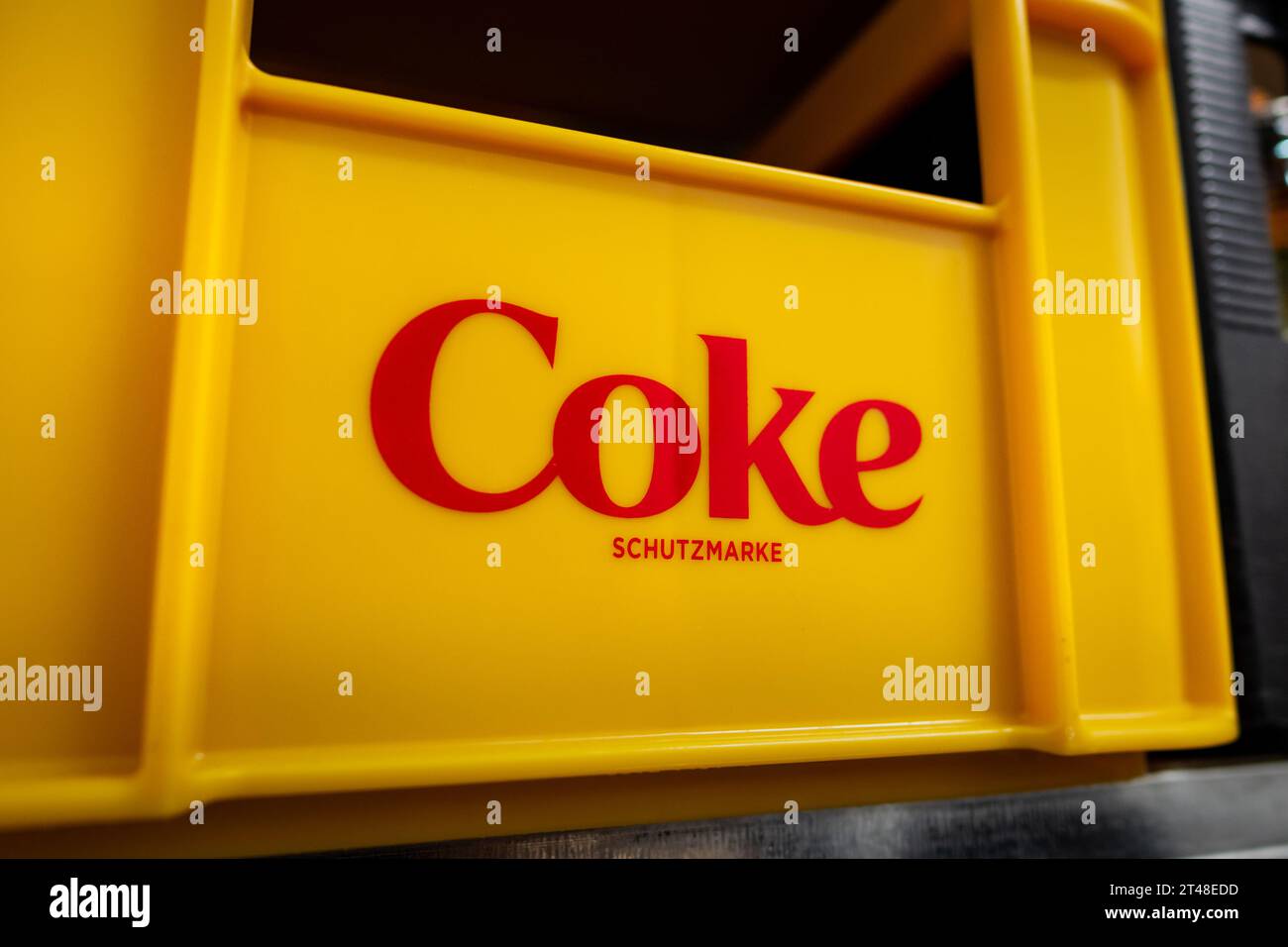 Coke-Logo-Zeichen der Firma Coca Cola auf einer gelben Kiste. Die Marke des beliebten Getränks ist eine eingetragene Marke. Stockfoto