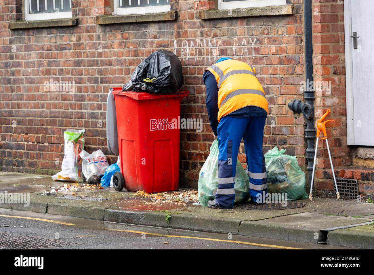 Ein Mitarbeiter des stadtrates räumt in einer Straße im Stadtzentrum von Middlesbrough, Großbritannien, die Straßenreinigung in überfüllten Mülltonnen auf. Stockfoto