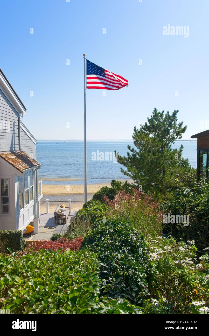 Die amerikanische Flagge weht am Pol unter hellblauem Himmel zwischen Cod-Cod-Landhäusern am Strand am Hafen von Provincetown Stockfoto