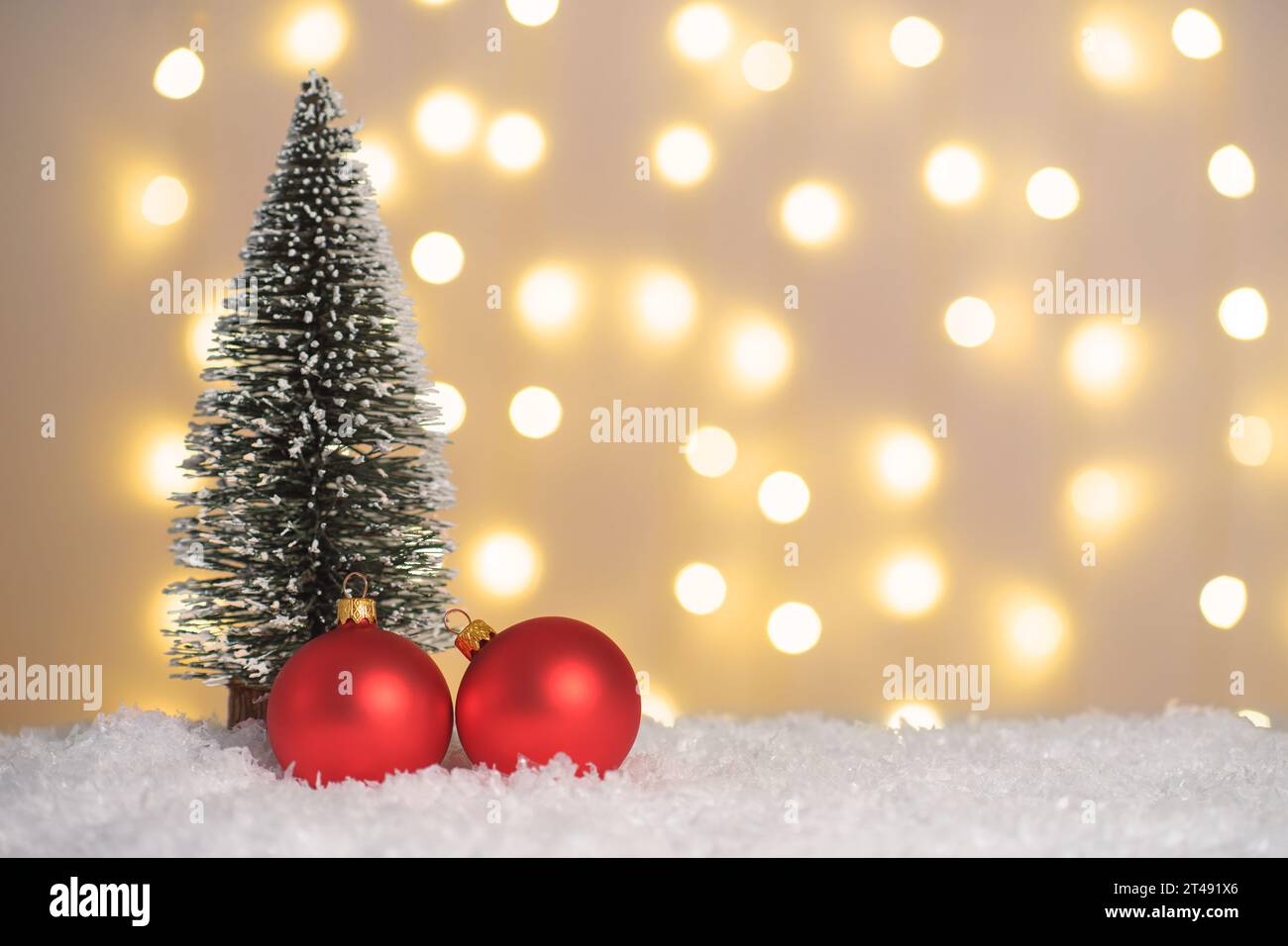 Weihnachtsbaum und zwei rote Kugeln auf Schnee und leuchtenden Lichtern Bokeh Hintergrund. Weihnachten, Neujahr Grußkarte mit Kopierraum. Weihnachtsbeleuchtung, Stockfoto