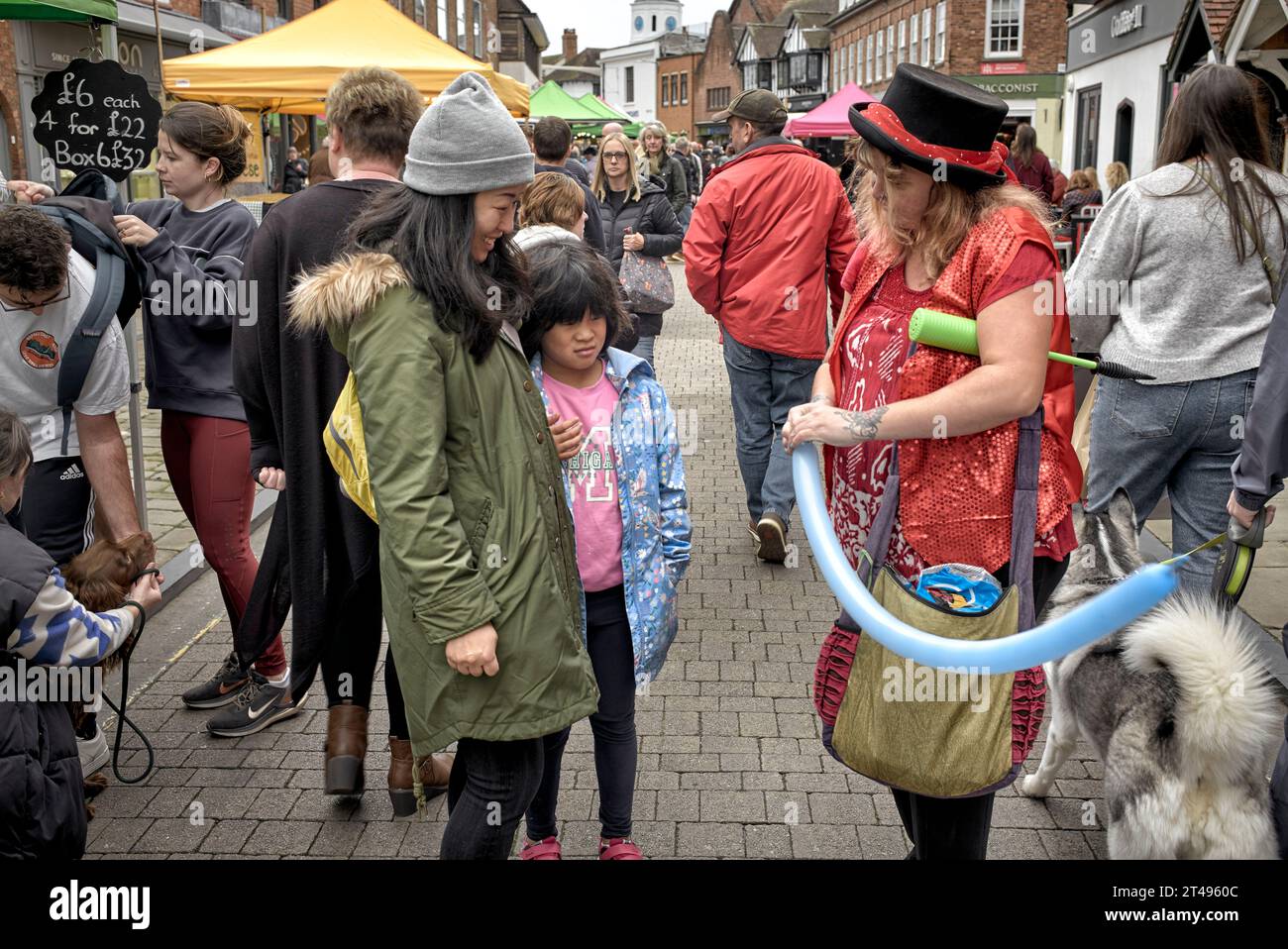 Weibliche Straßenunterhalterin formt einen Ballon für eine asiatische Mutter und ein Kind. England Großbritannien Stockfoto