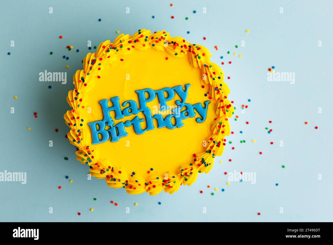 Gelbe Geburtstagskuche mit blauem Happy Birthday Gruß und Zuckerstreuseln auf blauem Hintergrund Stockfoto