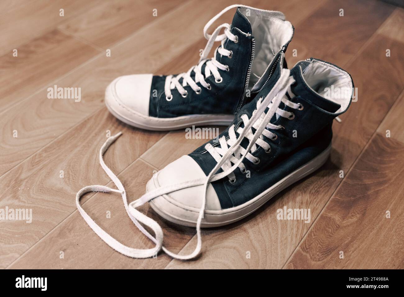 Lässiger modischer klassischer Hipster-Jugendschuh. Hohe schwarze, stylische Sneakers mit Gummisohlen und langen, nicht gebundenen Schnürsenkeln stehen auf dem Boden Stockfoto