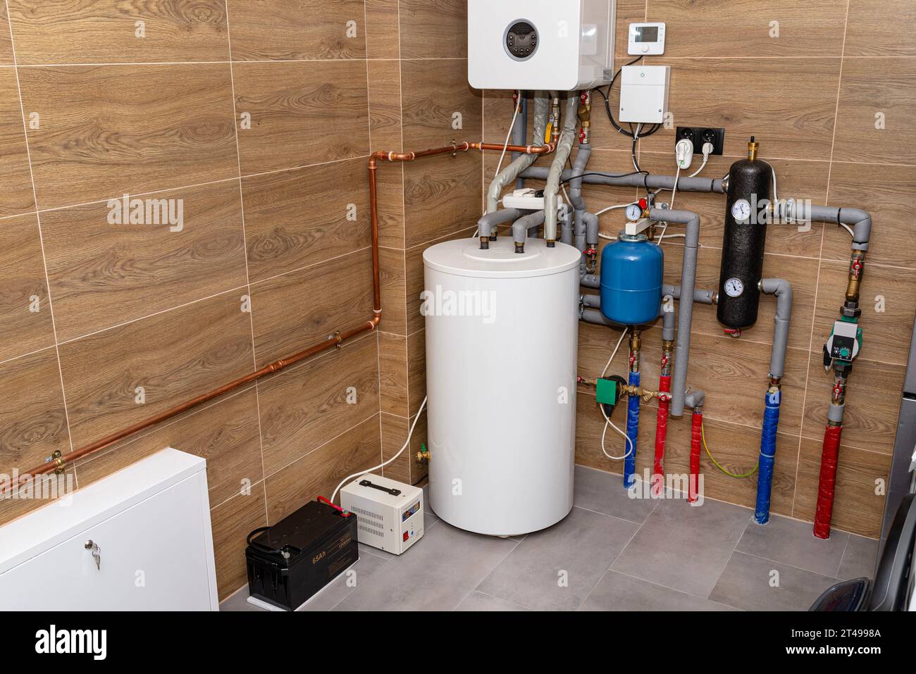 Moderner Gaskesselraum mit Holzkeramikfliesen, sichtbare Notstromversorgung mit 12-Volt-Batterie. Stockfoto