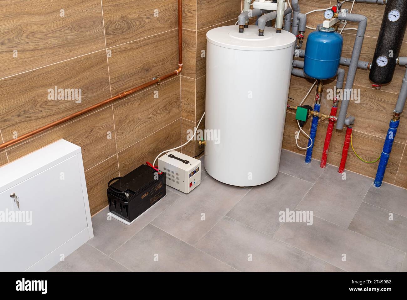 Moderner Gaskesselraum mit Holzkeramikfliesen, sichtbare Notstromversorgung mit 12-Volt-Batterie. Stockfoto