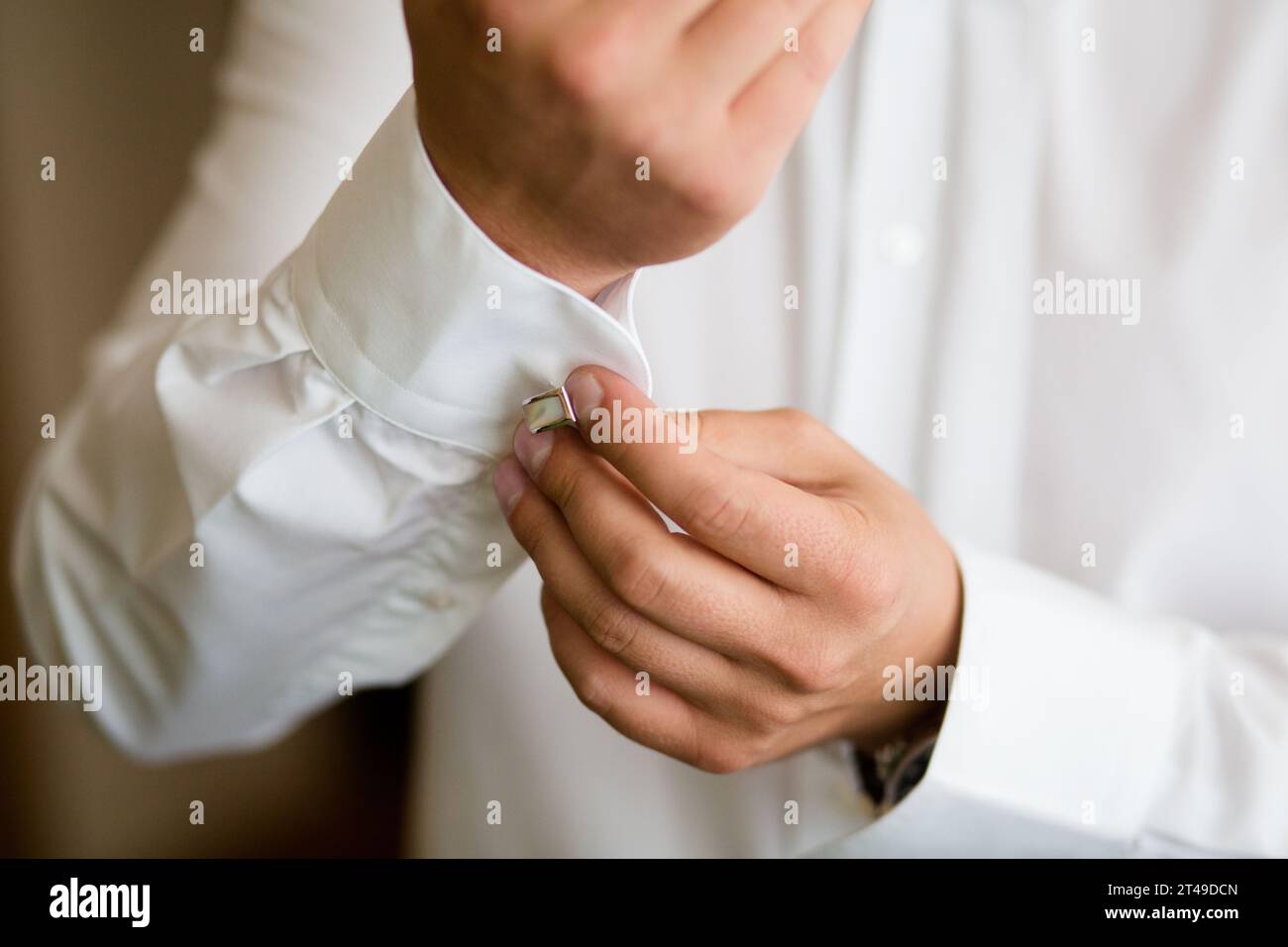 Nahaufnahme der Hände, die einen silbernen Manschettenknopf an einem weißen Hemd sichern. Eleganz und Vorbereitung unter natürlichem Licht. Stockfoto