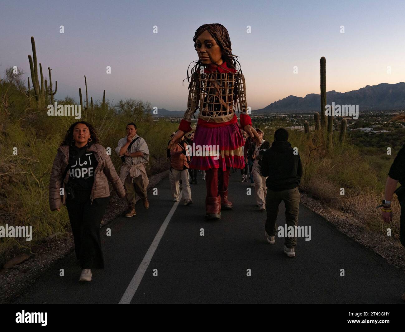 Tucson, Arizona, USA. Oktober 2023. Eine entschlossene kleine Amal, die 12 Fuß große Marionette eines 10-jährigen syrischen Flüchtlingsmädchens, macht sich bei Sonnenaufgang auf den Tumamoc Hill. Das Land ist heilig für einheimische indigene Stämme, die es vor mehr als 2000 Jahren besiedelten. Tumamoc ist Tohono O'Odham für die königliche Horneidechse, die Form des Berges. (Credit Image: © Sue Dorfman/ZUMA Press Wire) NUR REDAKTIONELLE VERWENDUNG! Nicht für kommerzielle ZWECKE! Stockfoto