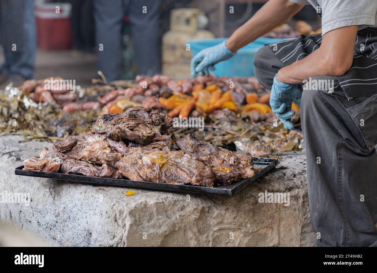 Ein Mann legt das Fleisch beiseite und legt es auf ein Tablett, das im Rahmen der Curanto-Zeremonie zubereitet wurde, ein traditionelles Essen aus Patagonien. Stockfoto