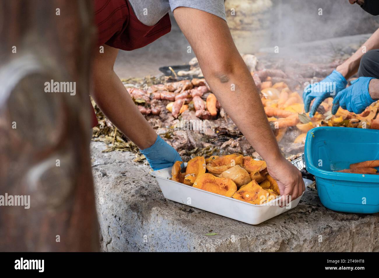 Ein Koch hält ein weißes Tablett mit Kürbisstücken, die unterirdisch als Teil der Zeremonie von Curanto, einem traditionellen Gericht aus Patagonien, zubereitet werden. Colonia Suiza, Stockfoto