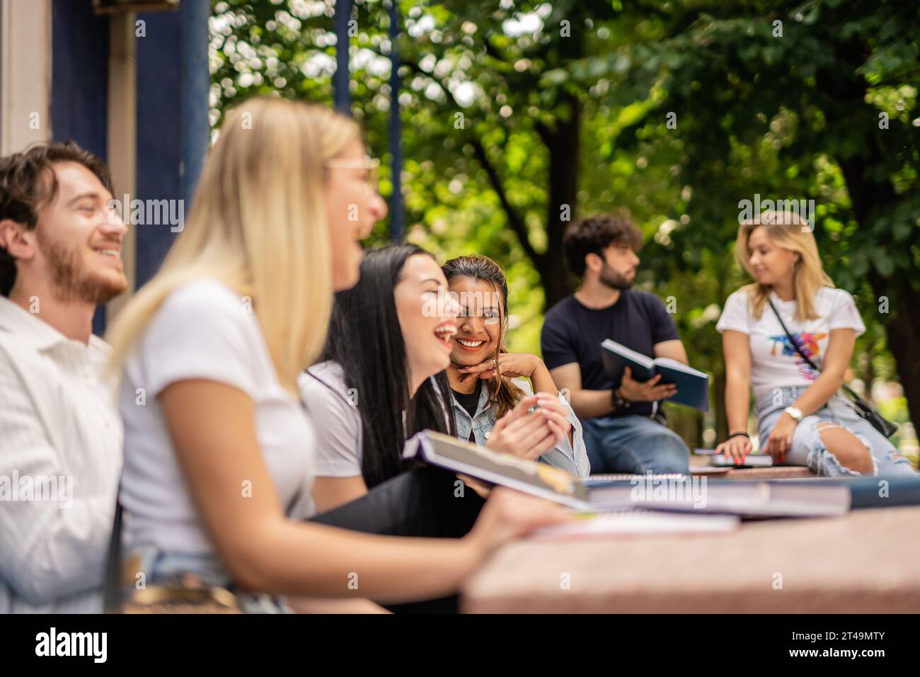 Glückliche Studenten, die Spaß während der Pause auf dem College-Hof haben, am Tisch sitzen Stockfoto