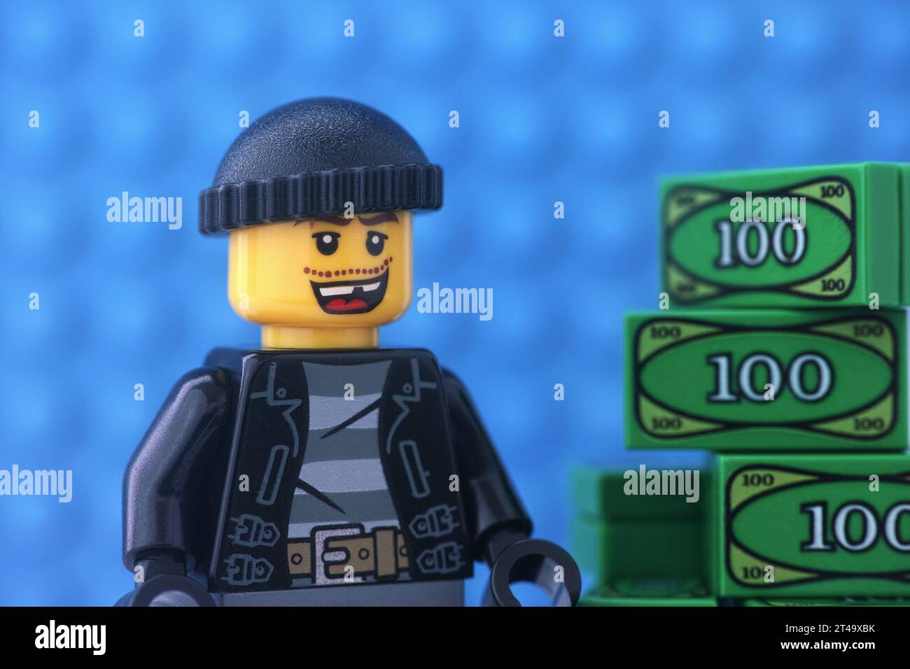 Tambow, Russische Föderation - 29. Oktober 2023 Eine Minifigur eines Lego-Einbrechers, die neben einem Geldhaufen vor einem blauen Hintergrund steht Stockfoto