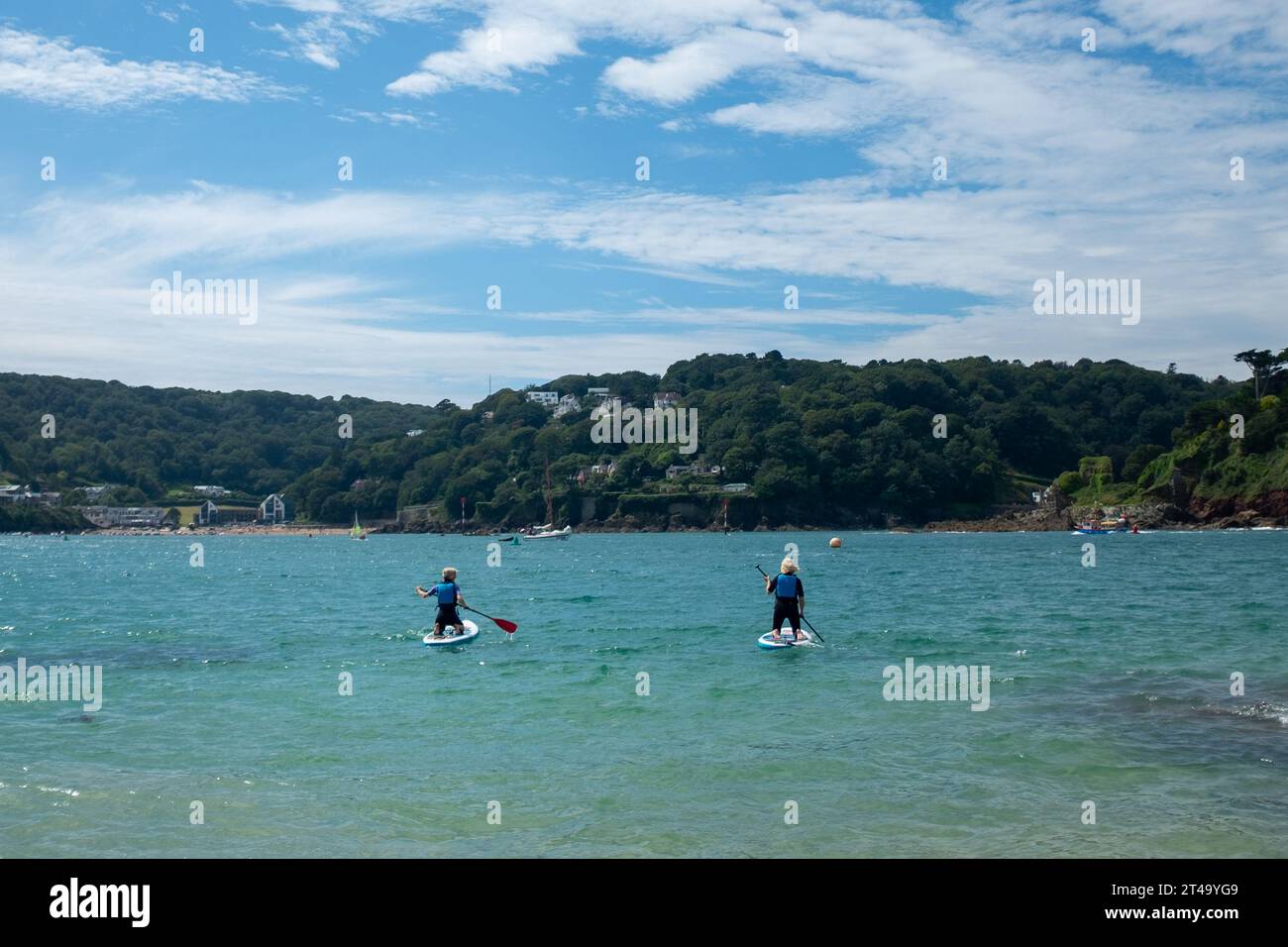 Zwei Paddelboarder fahren am Sunny Cove Beach, East Portlemouth, an einem Sommertag mit blauem Himmel in Richtung North und South Sands, Salcombe. Stockfoto