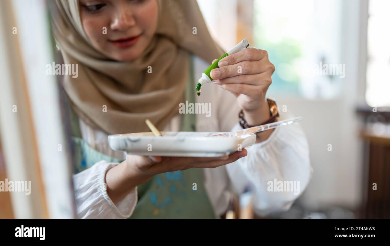 Nahaufnahme einer professionellen und talentierten asiatisch-muslimischen Künstlerin, die Farben auf einer Palette mischt und ihr Kunstwerk in ihrem Studio kreiert. Stockfoto