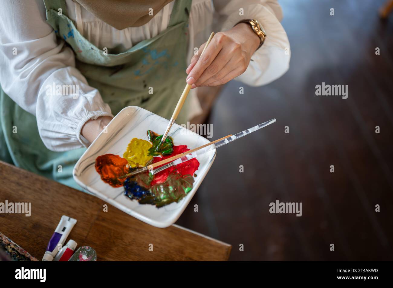 Draufsicht einer professionellen und talentierten Künstlerin, die Farben auf einer Palette mischt und ihr Kunstwerk in ihrem Studio kreiert. Stockfoto