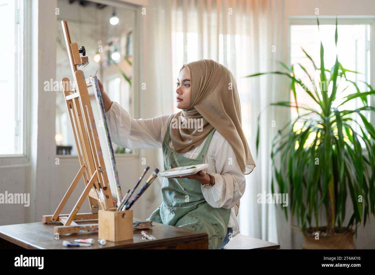 Eine konzentrierte und kreative asiatisch-muslimische Künstlerin, die ihre Kunstwerke, Zeichnungen oder Gemälde auf Leinwand in ihrem Atelier-Atelier kreiert. Stockfoto