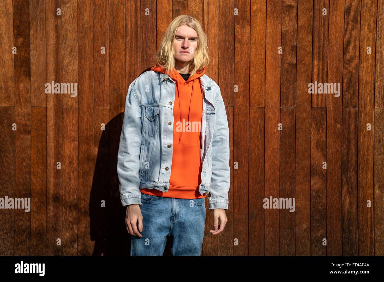 Apathischer blonder langer Haar Mann skandinavisches androgynes Aussehen steht in der Nähe von Holzzaun. Stockfoto