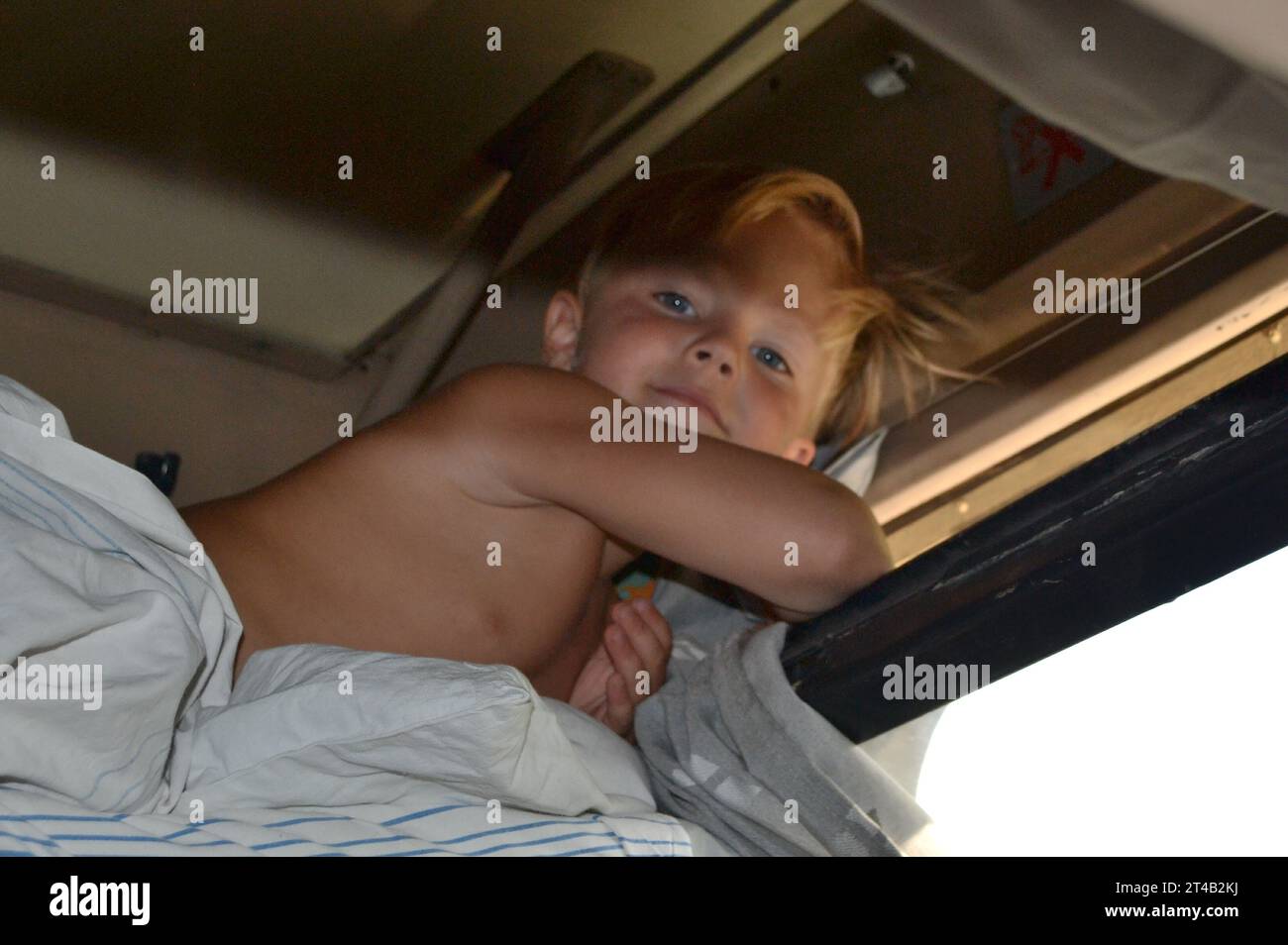 Ein kleiner neugieriger Junge, der nach dem Schlaf ins Fenster schaut, Innenaufnahme. Der kleine Junge fährt mit dem Zug und blickt durch das Fenster. Hoch Stockfoto