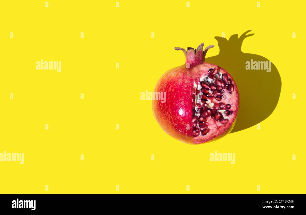 Rote Granatapfelfrucht auf hellgelbem Hintergrund mit Kopierraum. Minimales Konzept. Kreative Idee für gesunde Lebensmittel. Granatapfel-ästhetischer Hintergrund. Stockfoto