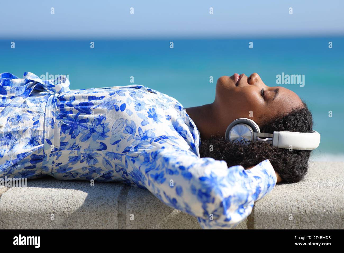 Profil einer schwarzen Frau, die Kopfhörer trägt und am Strand Musik hört Stockfoto