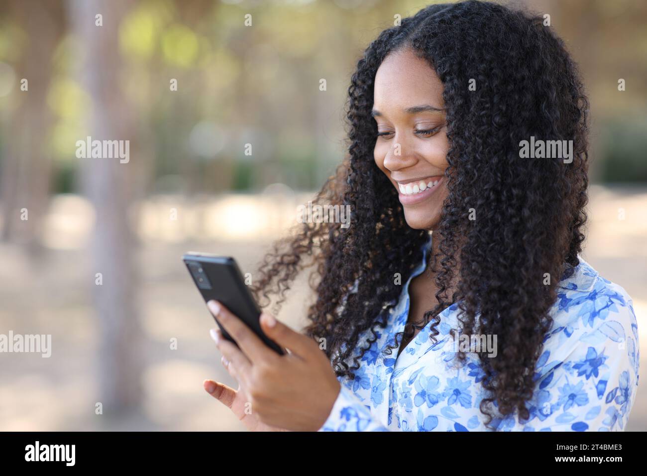 Glückliche schwarze Frau, die ihr Handy lächelt und in einem Park läuft Stockfoto