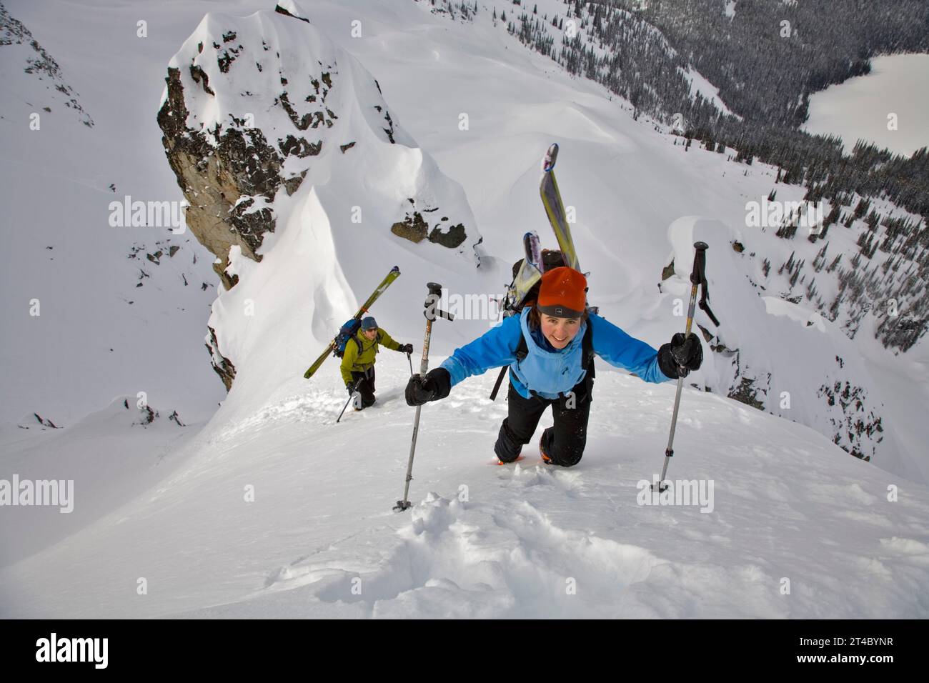 Frau, die die Schneehänge mit Skiern auf dem Rucksack hinaufwandert, British Columbia, Kanada Stockfoto