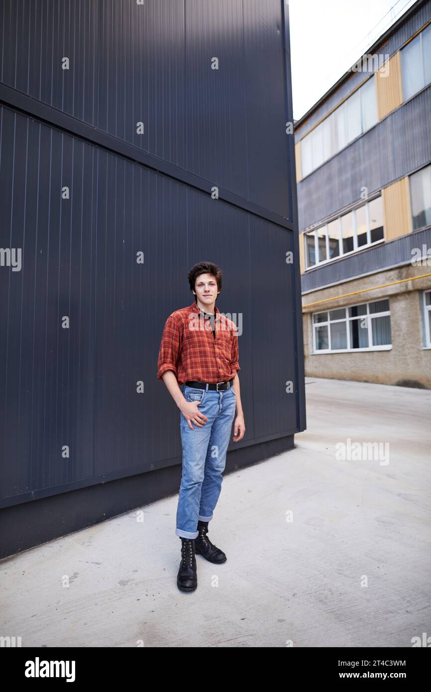 Lächelnder junger Mann, der im Innenhof des Campus vor einer grauen Mauer steht Stockfoto