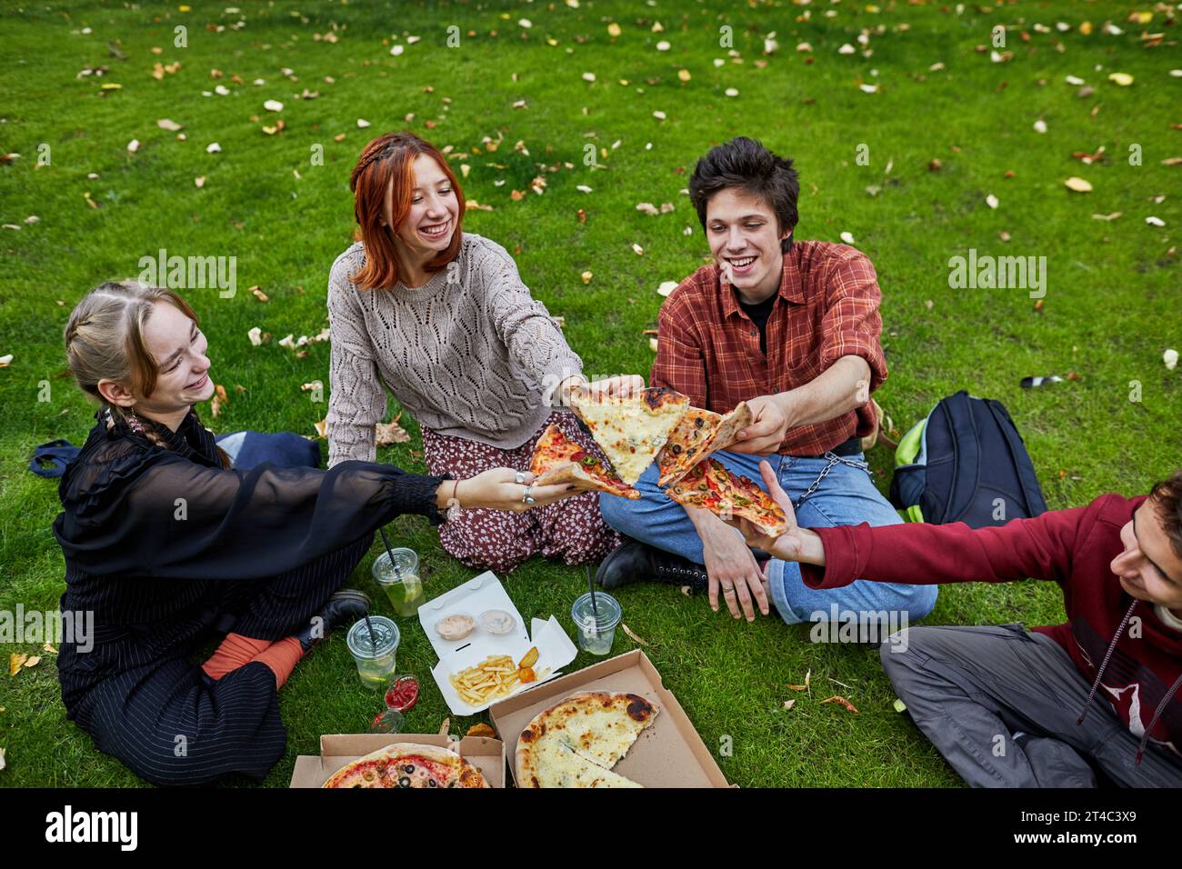 Eine Gruppe junger Leute lacht und isst Pizza auf dem Rasen Stockfoto