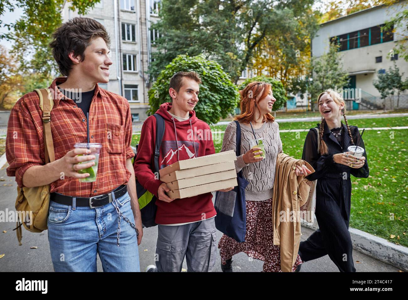 Glückliche junge Leute, die auf der Straße mit Pizza und Getränken spazieren gehen Stockfoto