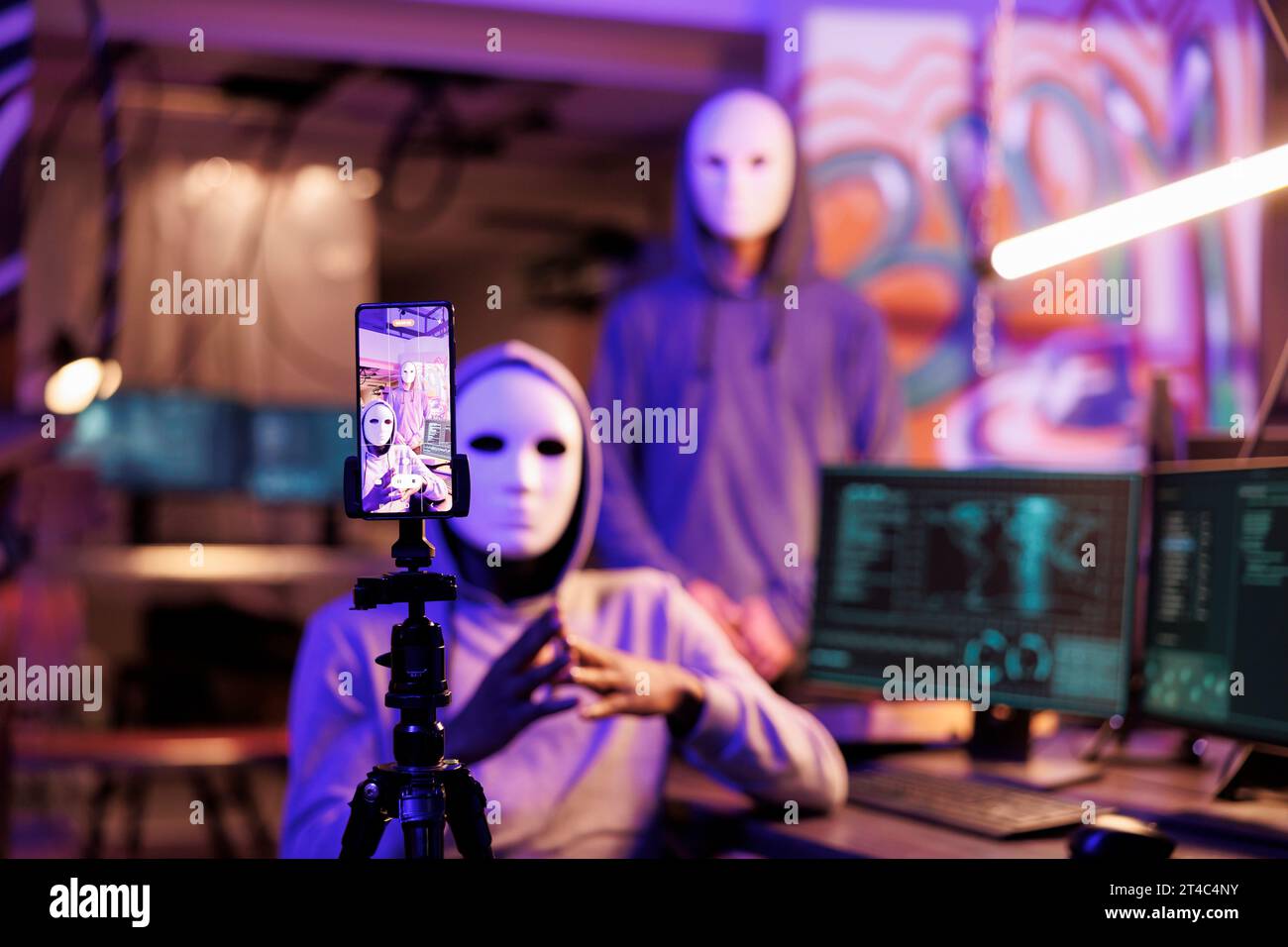 Mobiltelefon-Bildschirm, auf dem anonyme Hackeraufzeichnungsnachrichten angezeigt werden. Internetkriminelle in Masken und Hauben streamen nachts in einem verlassenen Lagerhaus live auf dem Smartphone Stockfoto