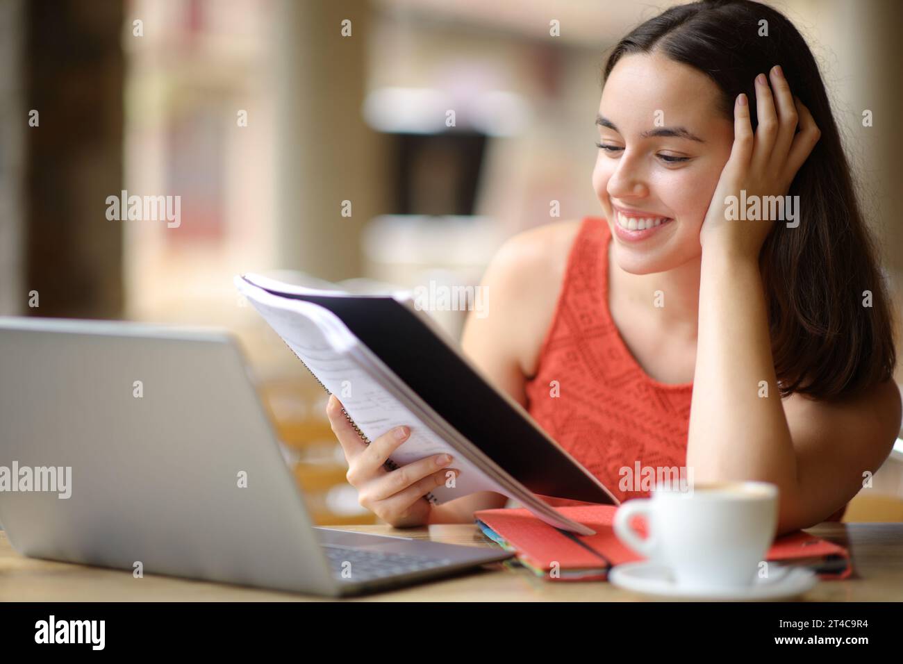 Glücklicher Student, der Notizen mit Laptop auf der Terrasse eines Coffee-Shops vergleicht Stockfoto
