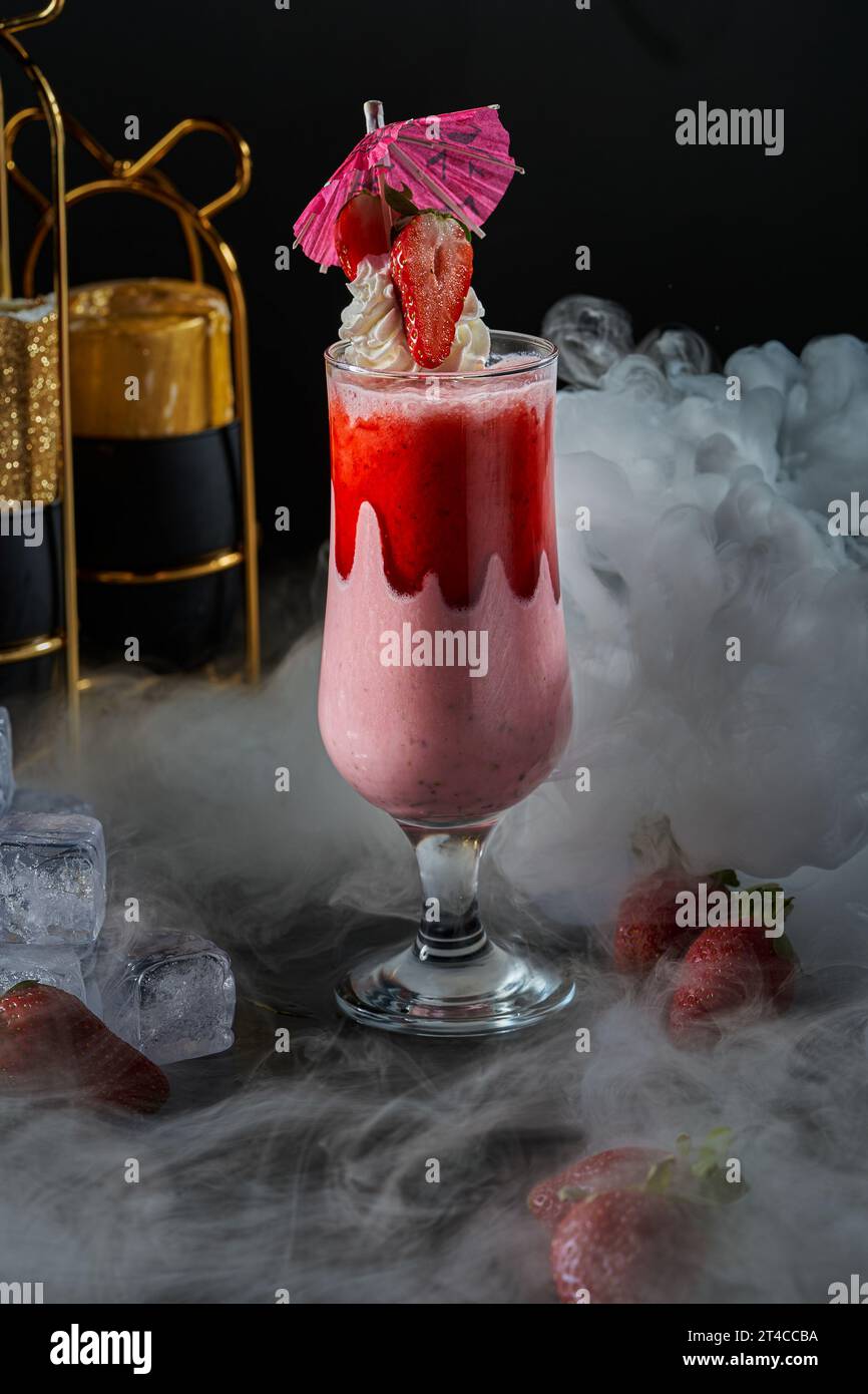 Bild eines Glases Milch- und Erdbeercocktail auf schwarzem Hintergrund mit Raucheffekten Stockfoto