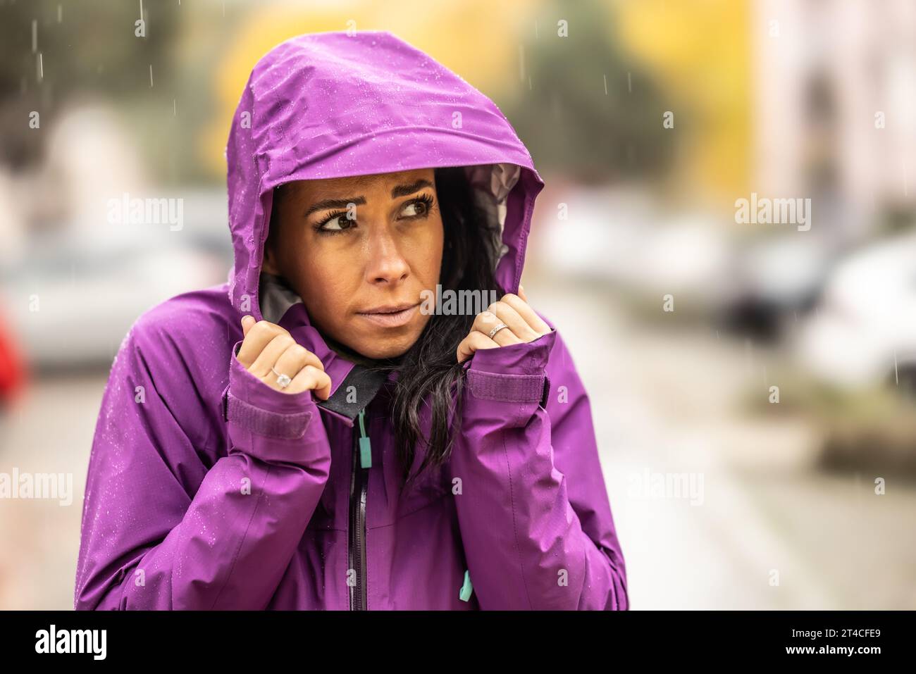 Eine gefrorene junge Frau in einer Regenjacke hat eine Kapuze und schutzt ihren Kopf im Spatherbst vor Regen und Wind Stockfotografie Alamy