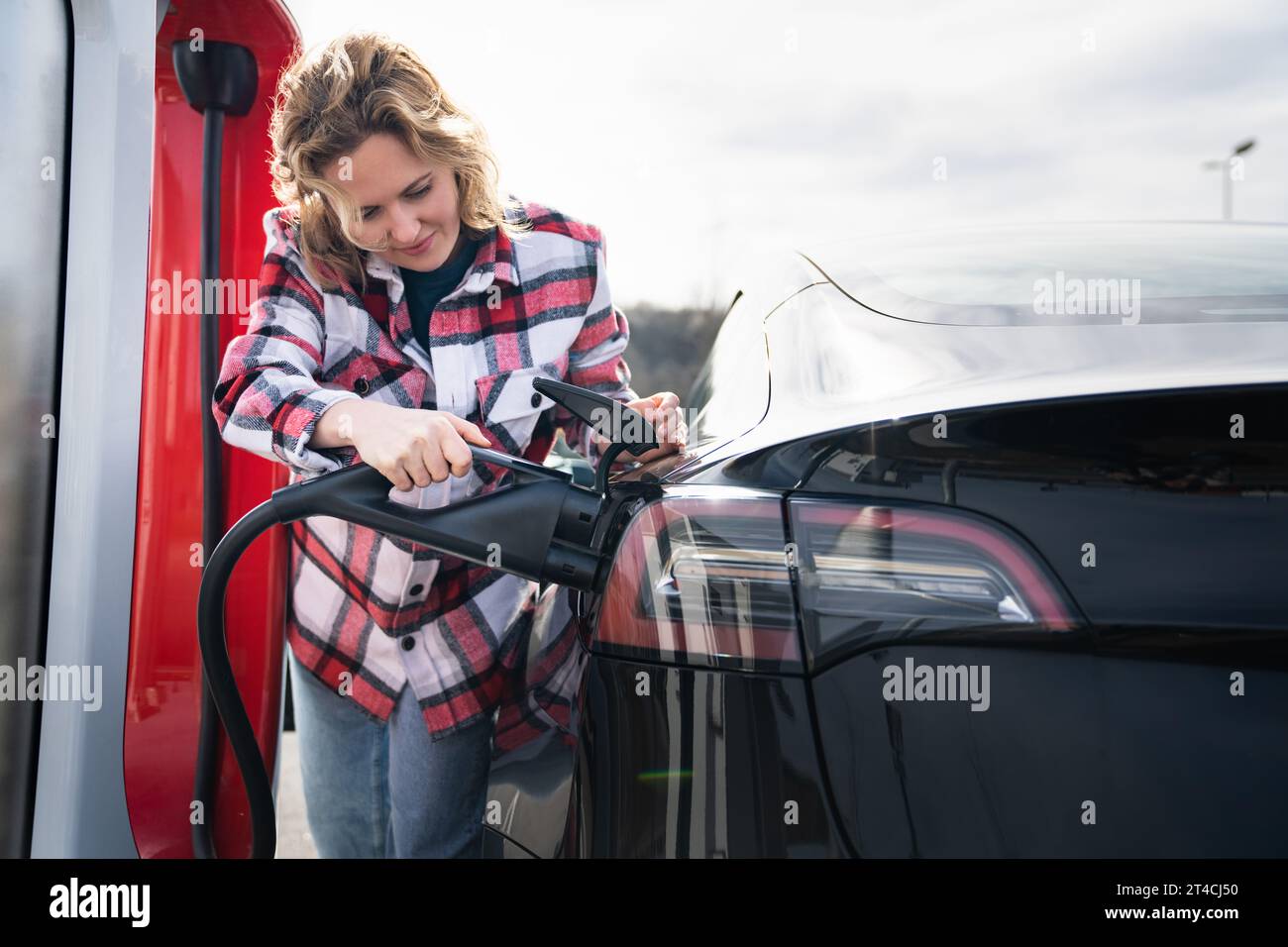 Eine Frau in einem karierten Hemd lädt ein Elektroauto auf. Stockfoto