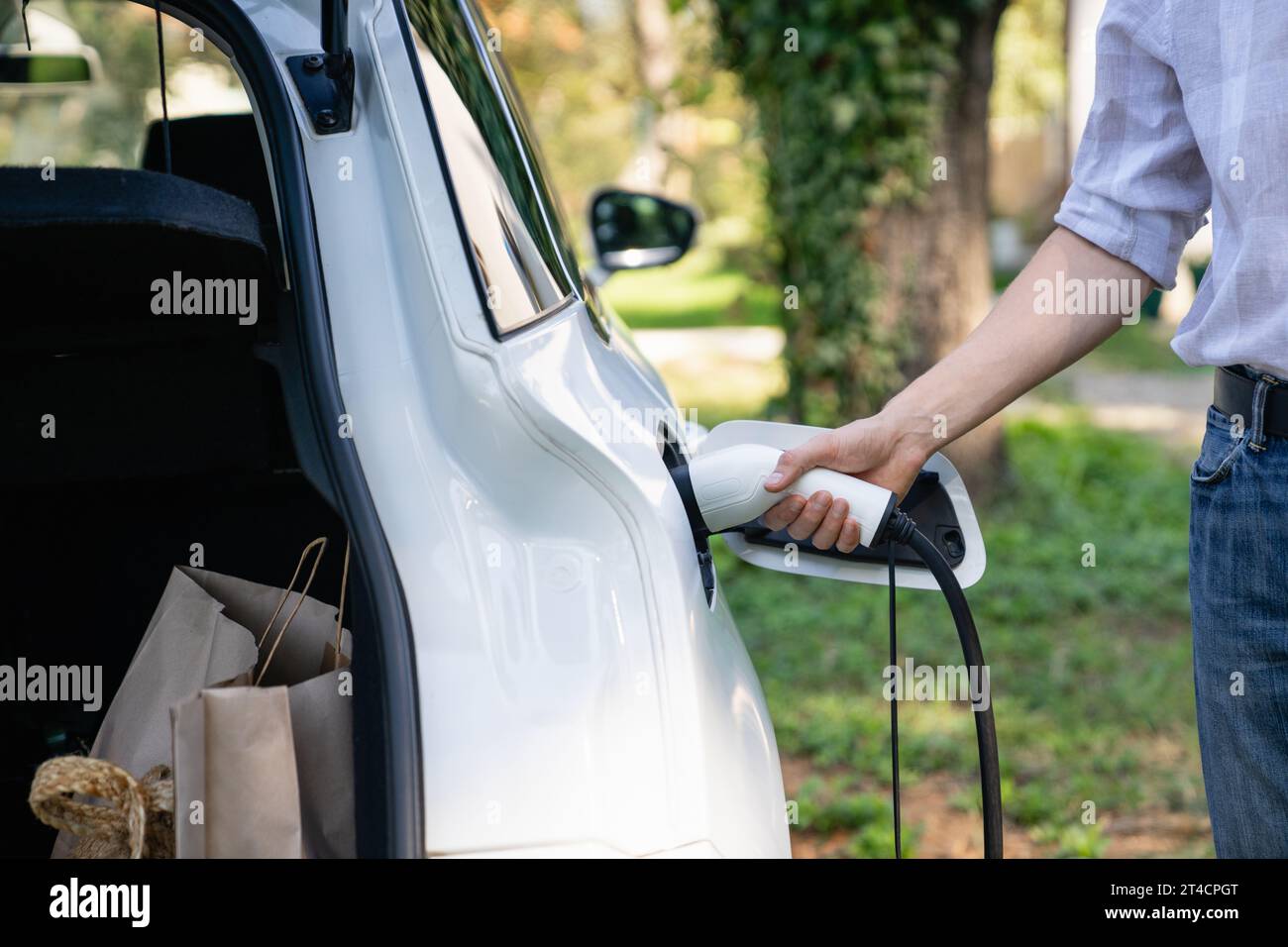 Ein Mann steht an einem Elektroauto und hält einen Ladestecker. Stockfoto