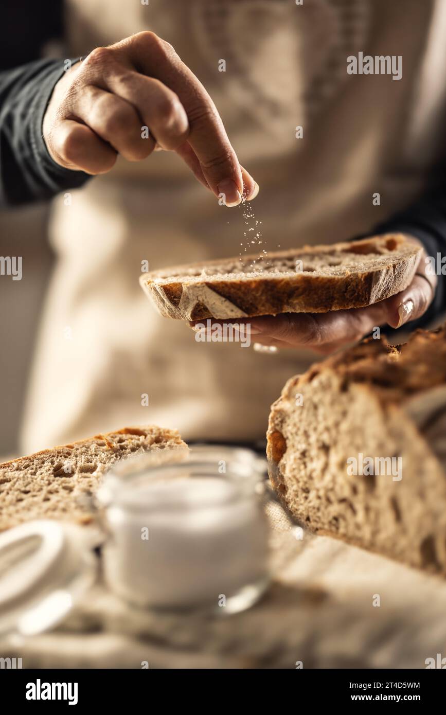 Weibliche Köchin salzt eine frische Scheibe Brot - Nahaufnahme. Stockfoto