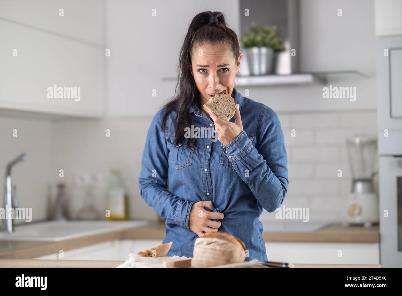 Frau kann kein Brot und Getreideprodukte essen wegen Gluten-Intoleranz. Eine junge Zöliakie leidet unter Bauchschmerzen, nachdem sie frisches Brot gegessen hat. Stockfoto
