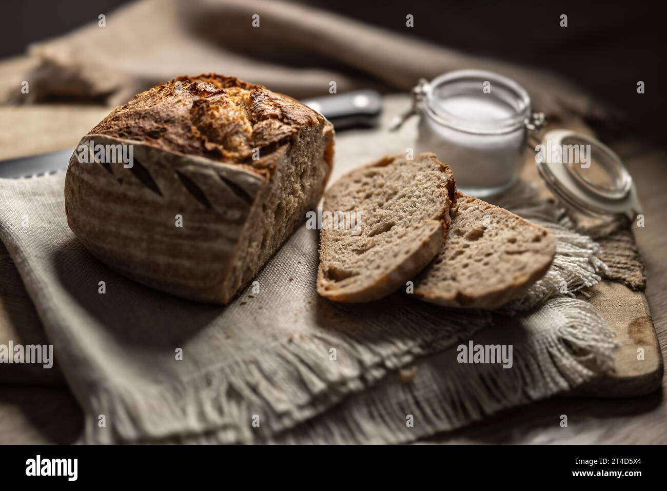 Frisches Sauerteigbrot mit einer geschnittenen Scheibe und Salz auf einem Schneidebrett. Stockfoto