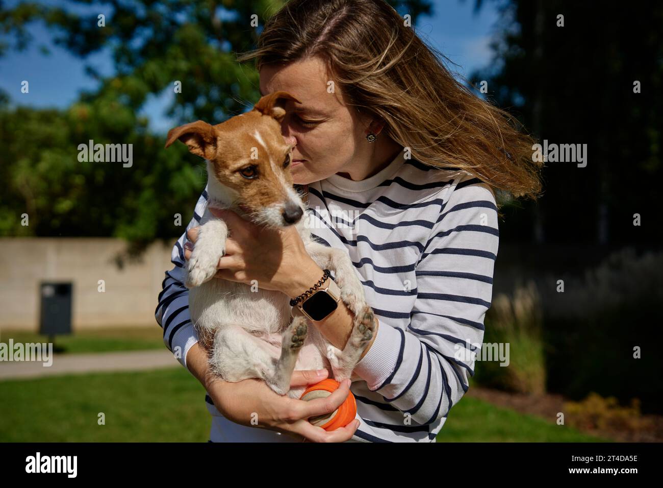 Die Frau hält ihren Hund an den Händen und umschließt ihn. Glückliche Besitzerin umarmt und küsst süße Freundin. Tierpflege Stockfoto