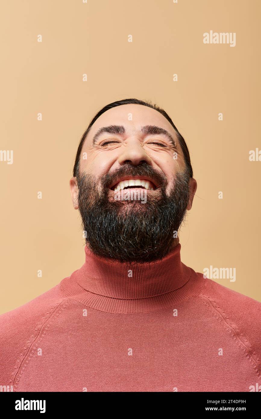 Lächelnder Mann mit Bart in rosa Rollkragenpullover, der fröhlich vor beigefarbenem Hintergrund lächelt Stockfoto