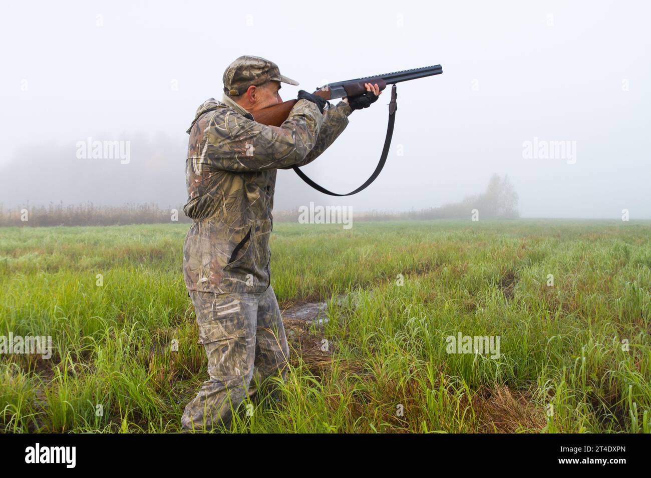 Ein Mann in Tarnung zielt mit einem Jagdgewehr auf einer Wiese an einem nebeligen Morgen Stockfoto