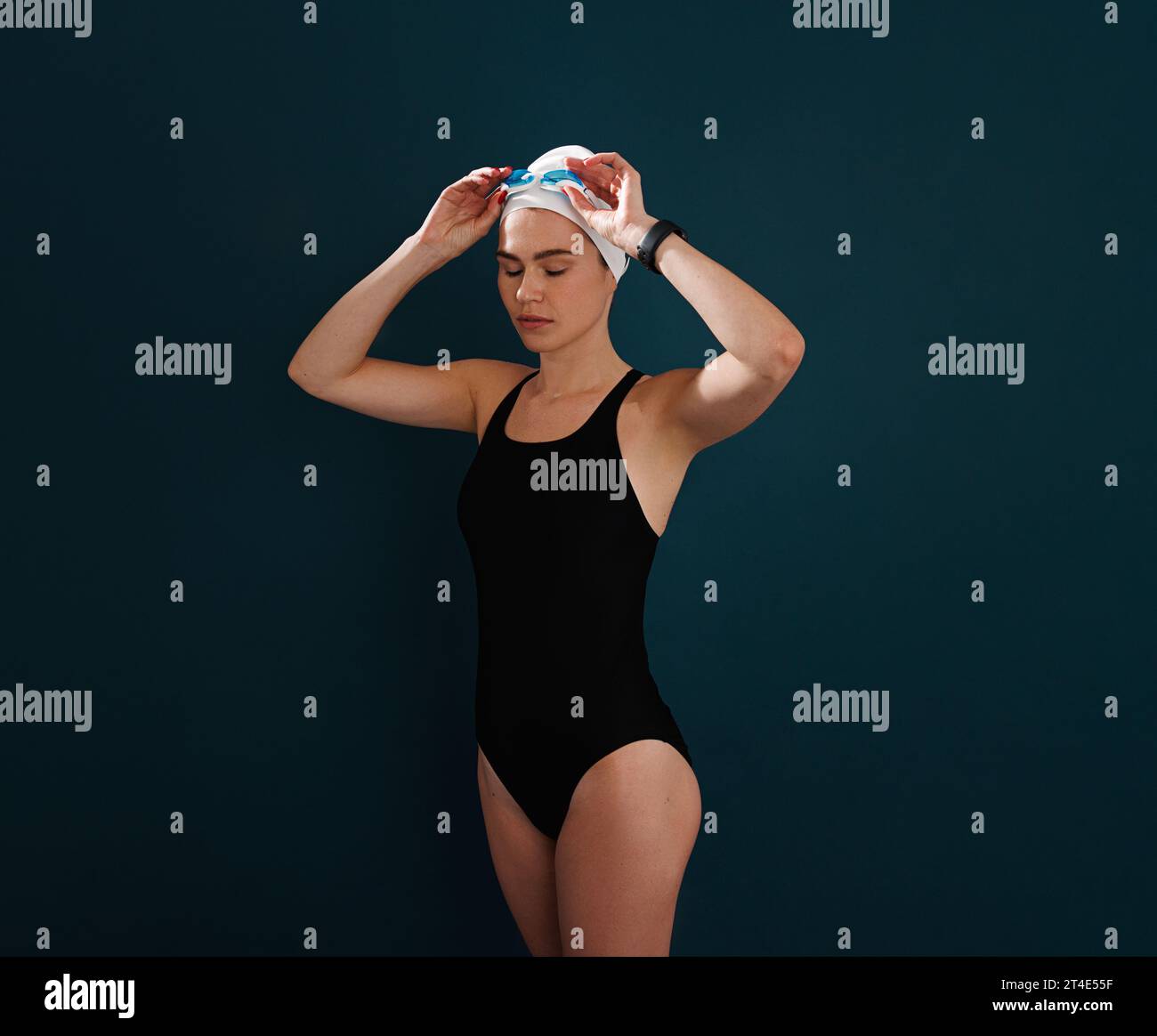 Junge schlanke professionelle Schwimmerin, die die Brille über blauem Hintergrund anpasst Stockfoto