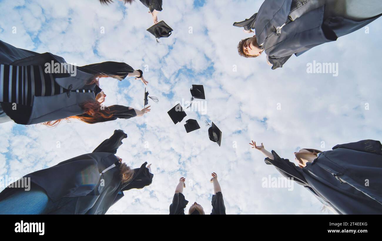Fröhliche Absolventen stehen im Kreis und werfen ihre Kappen hoch. Stockfoto