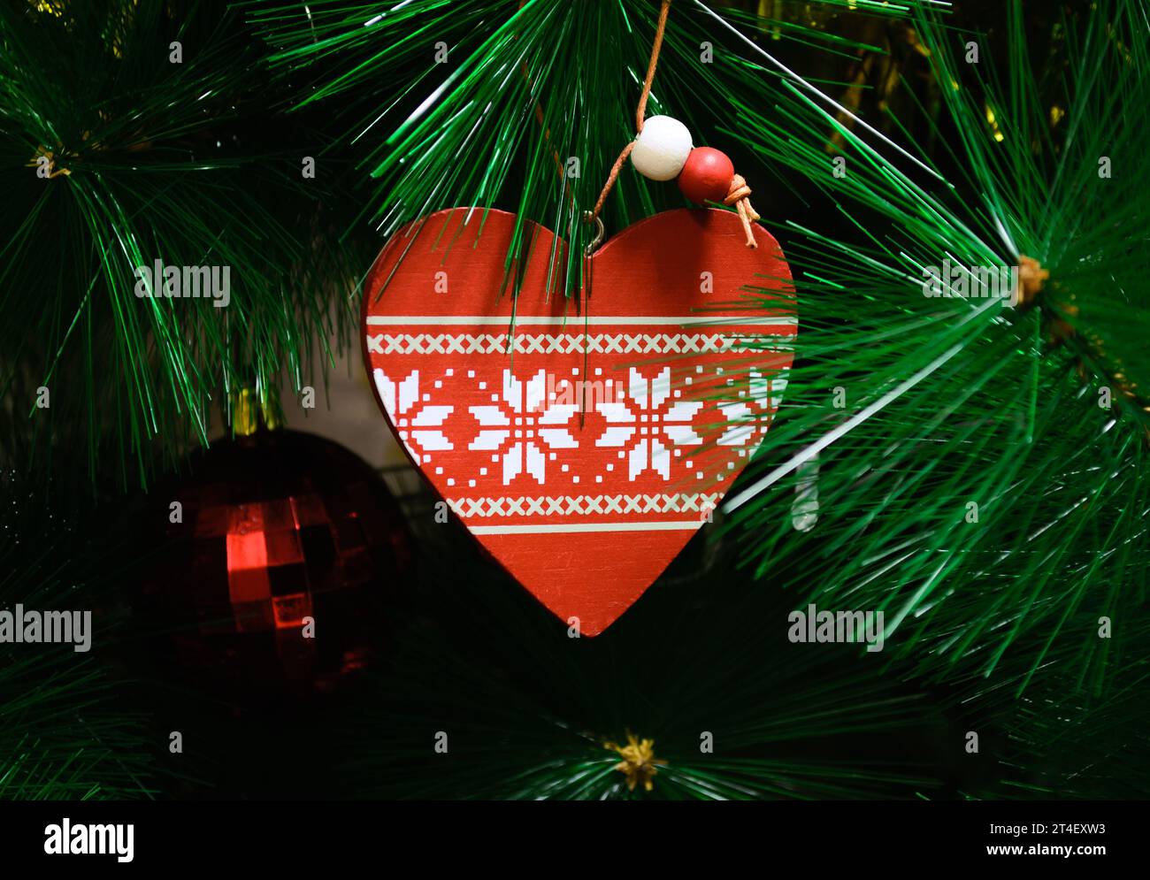 Ein Spielzeug in Form eines Herzens hängt vor dem Hintergrund grüner Zweige eines künstlichen Weihnachtsbaums Stockfoto