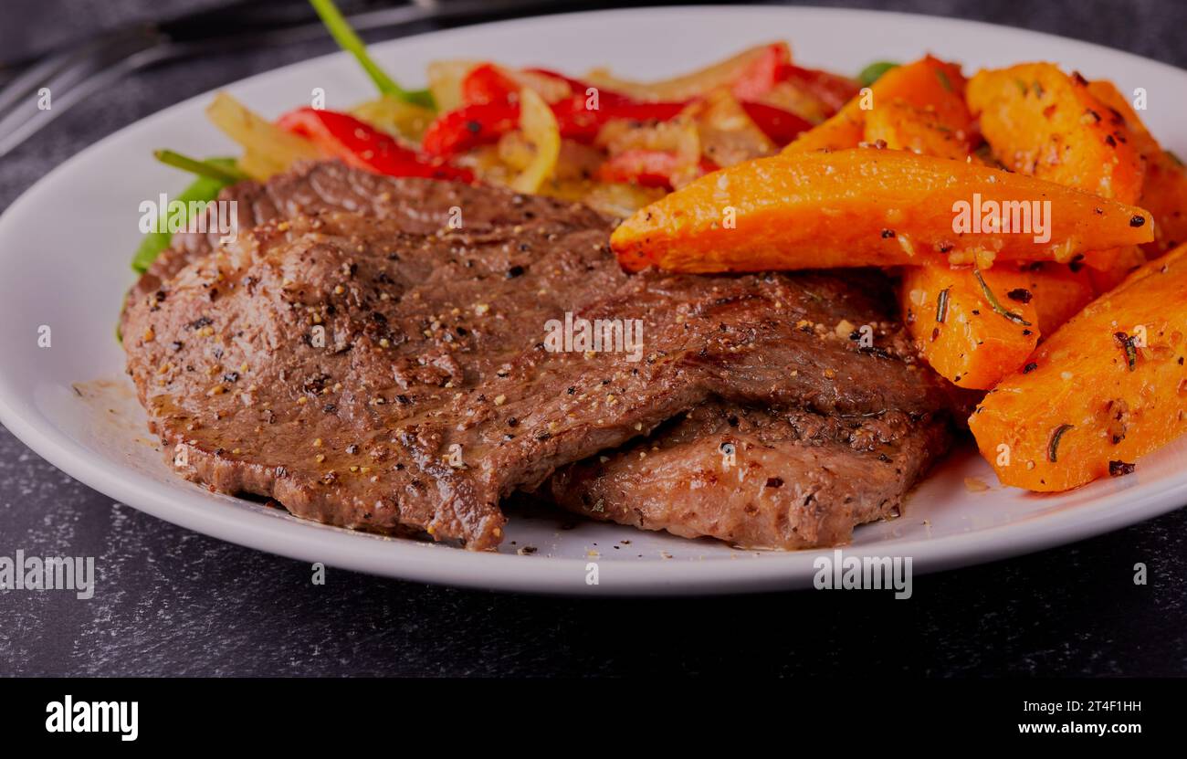 Dünn geschnittene Rindersteaks mit Süßkartoffelscheiben und gemischtem Spinatsalat. Stockfoto