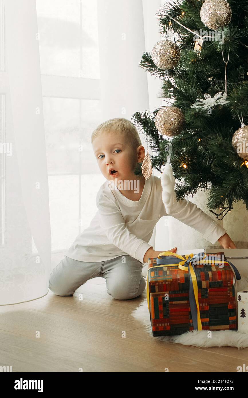 Der charmante Junge nimmt ein Weihnachtsgeschenk unter dem Neujahrsbaum Stockfoto