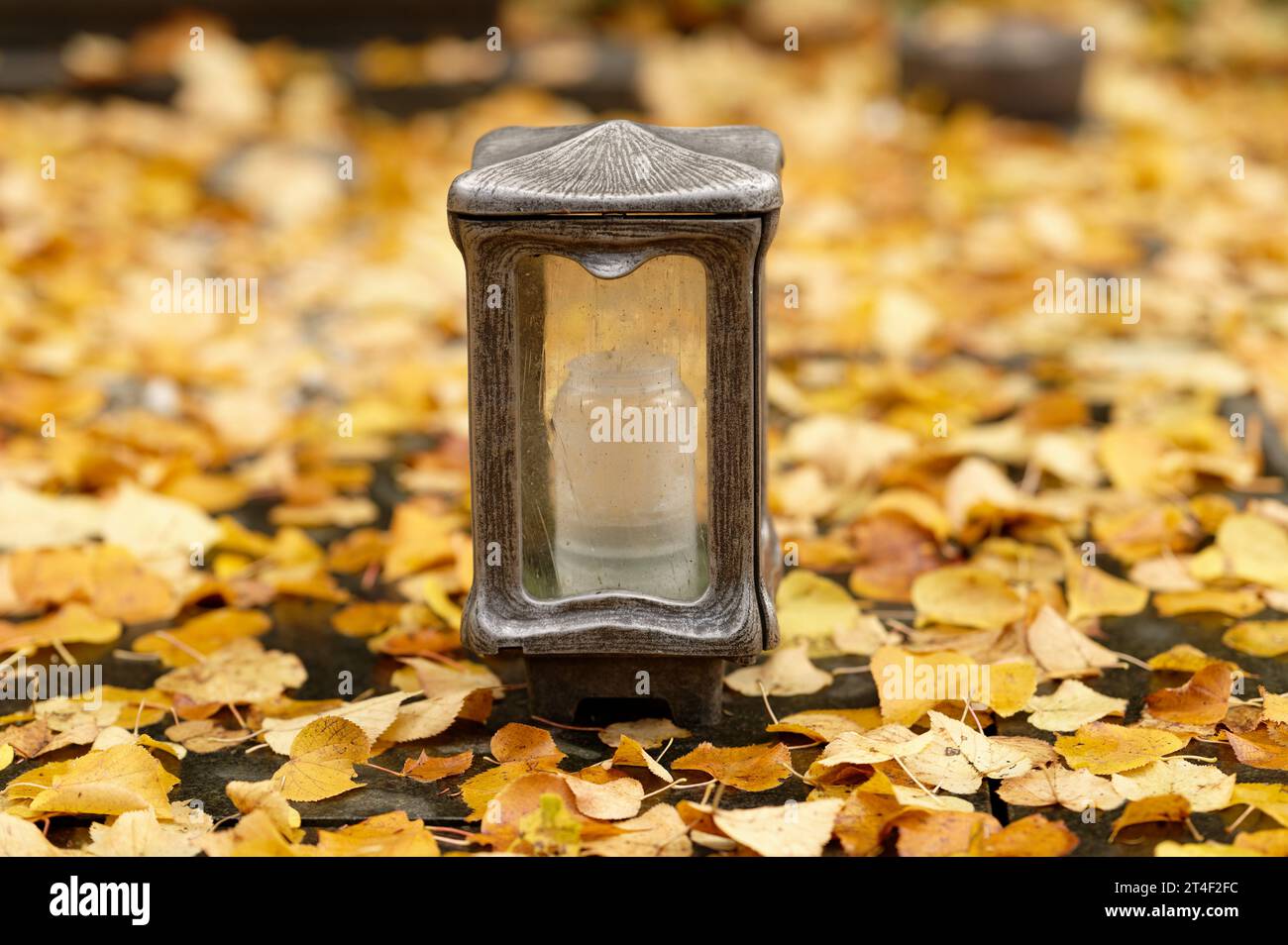 Eine Grablaterne auf einem mit Herbstlaub bedeckten Grab auf einem Friedhof im Herbst Stockfoto