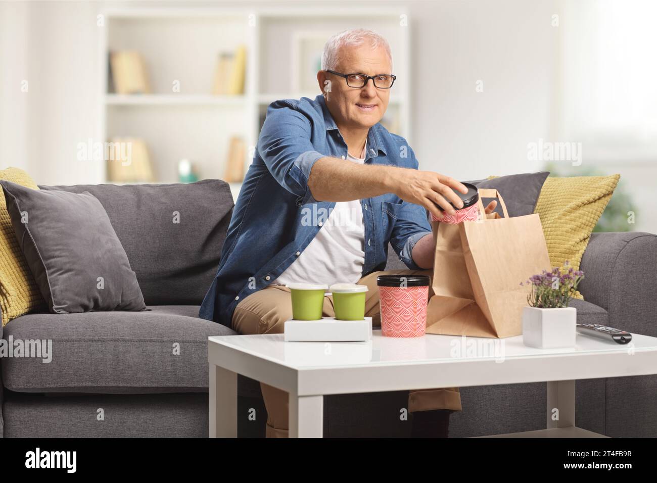 Ein reifer Mann sitzt zu Hause auf einem Sofa mit Essenskisten zum Mitnehmen auf einem Tisch Stockfoto