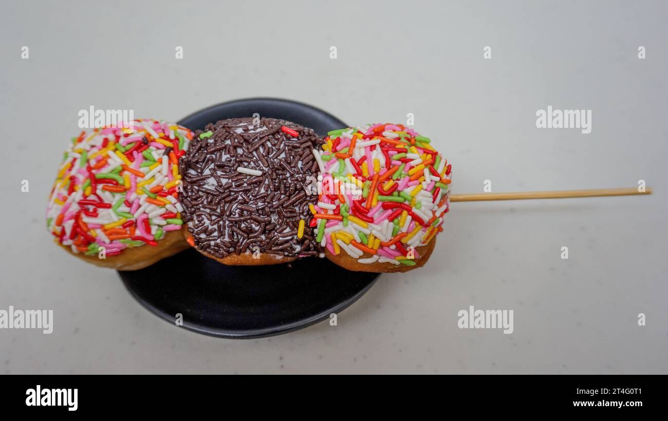 Donuts mit bunten Streuseln und Schokoladenstreusel auf Spießen wie Satay auf einem schwarzen Teller Stockfoto